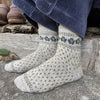 Gray socks with floral patterns worn by a person sitting on a wooden bench.