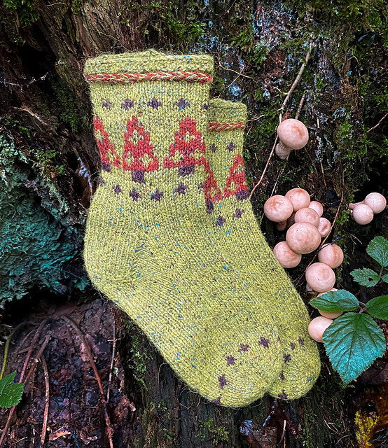 Knitted green sock with red and purple pattern on a tree stump with mushrooms