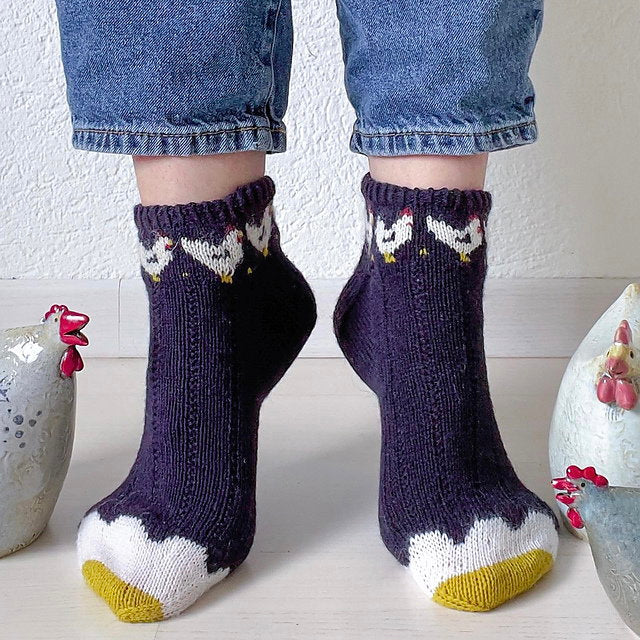 Person wearing dark purple socks with chicken designs on a light background