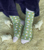 Green socks with white and yellow patterns worn by a person on a fluffy surface with small stuffed animals.