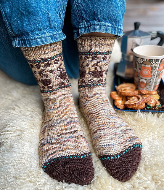 Person wearing patterned socks with a cozy background of a mug and cookies.