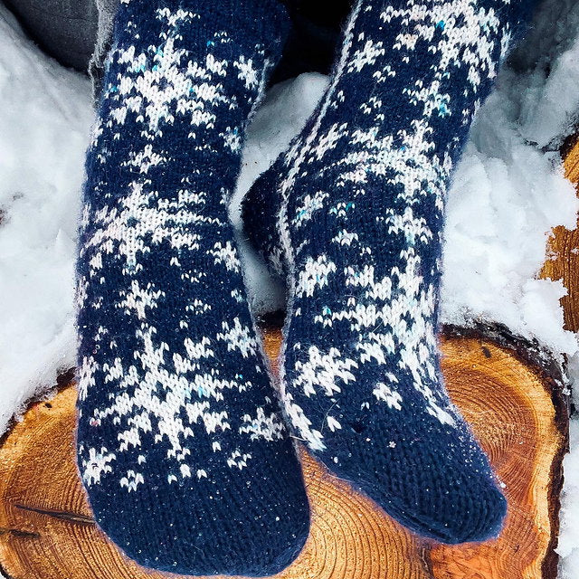 Blue and white patterned socks on a wooden log with snow in the background