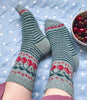 Pair of green and red patterned socks on feet with a bowl of cherries on a polka dot blanket.