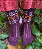 Purple patterned socks worn by a person standing on a forest floor.