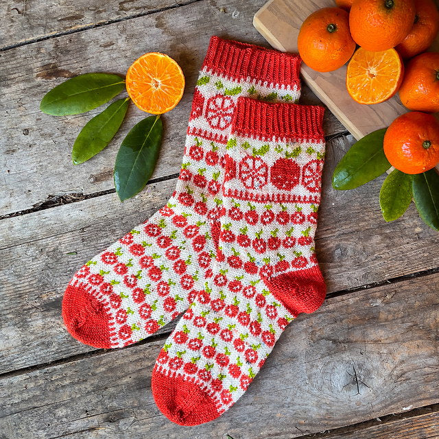 Knitted sock with orange pattern on a wooden surface with oranges and leaves.
