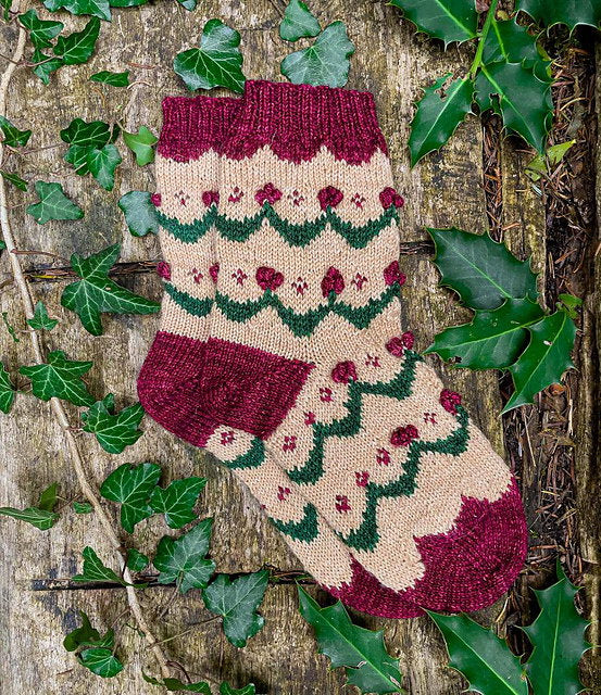 Knitted Christmas stocking with festive pattern on a wooden surface with ivy leaves.