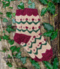 Knitted Christmas stocking with festive pattern on a wooden surface with ivy leaves.