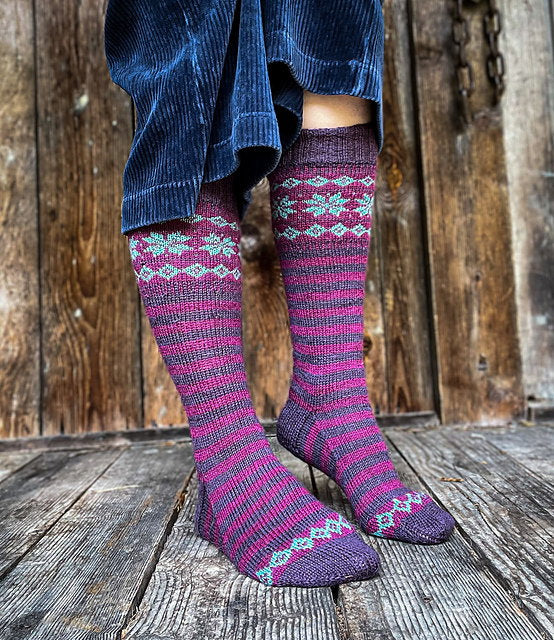 Person wearing patterned knee-high socks on a wooden floor with a wooden wall background