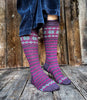 Person wearing patterned knee-high socks on a wooden floor with a wooden wall background