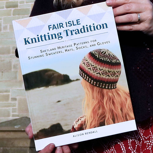 Book titled 'Fair Isle Knitting Tradition' held by a person with a scenic background