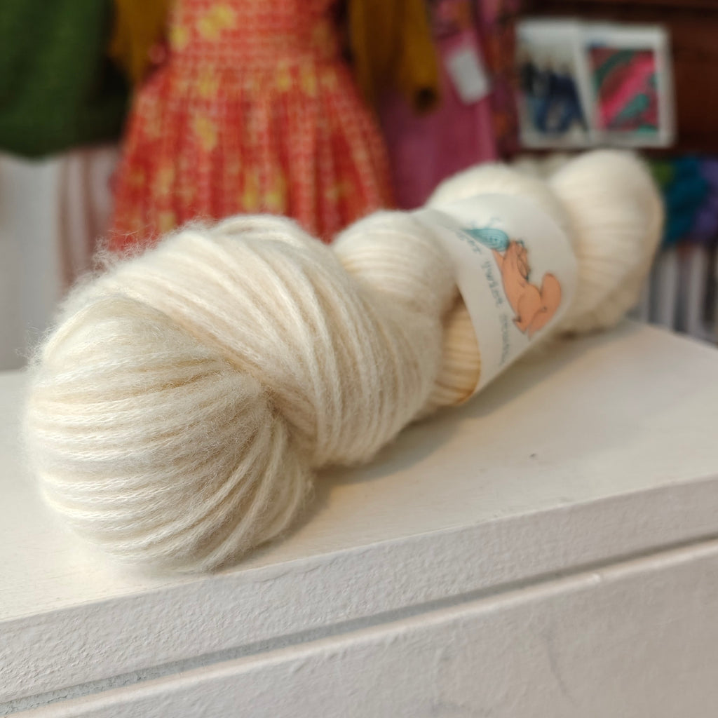 Ball of white yarn with a label on a white surface, with a blurred background
