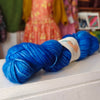 Blue skein of yarn with a label on a white surface, with colorful fabric in the background