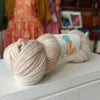 Two skeins of beige yarn with a label on a white surface, blurred background