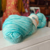 Turquoise yarn skein on a white surface with a blurred background