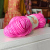 Pink yarn skein with a label on a white surface, blurred background