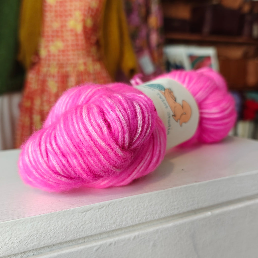 Pink yarn skein with a label on a white surface, blurred background