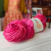 Two skeins of pink yarn on a white surface with a blurred background