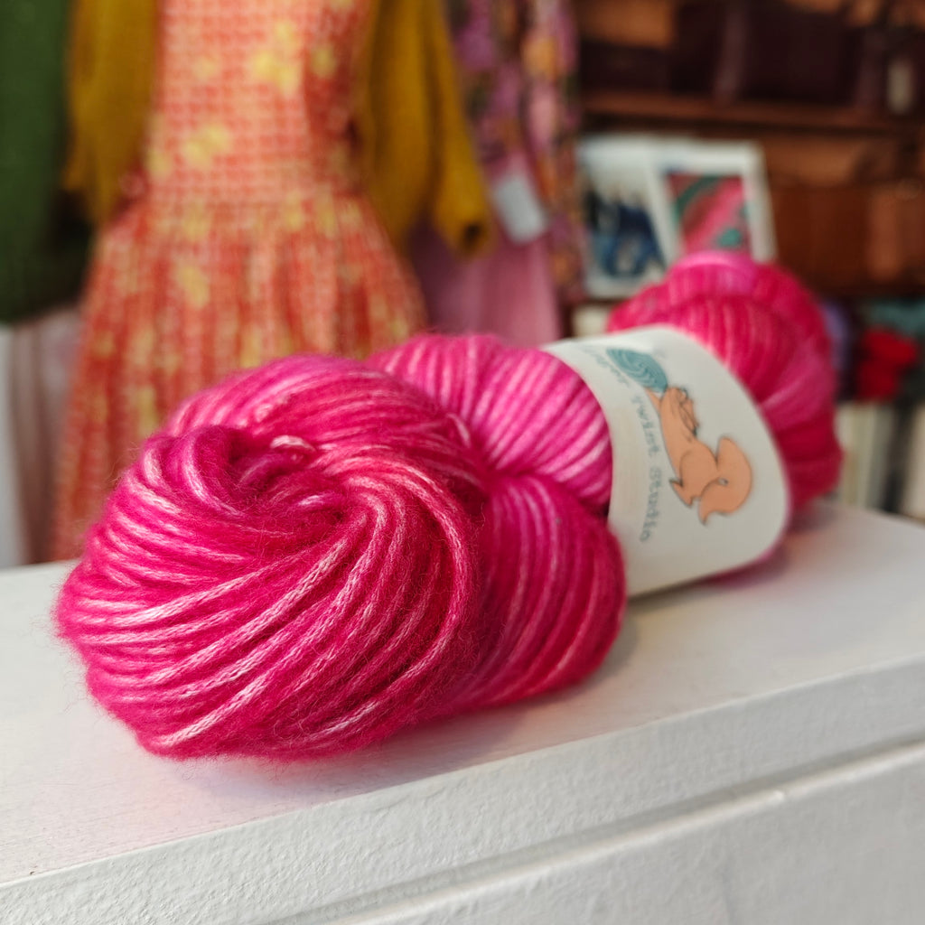 Two skeins of pink yarn on a white surface with a blurred background