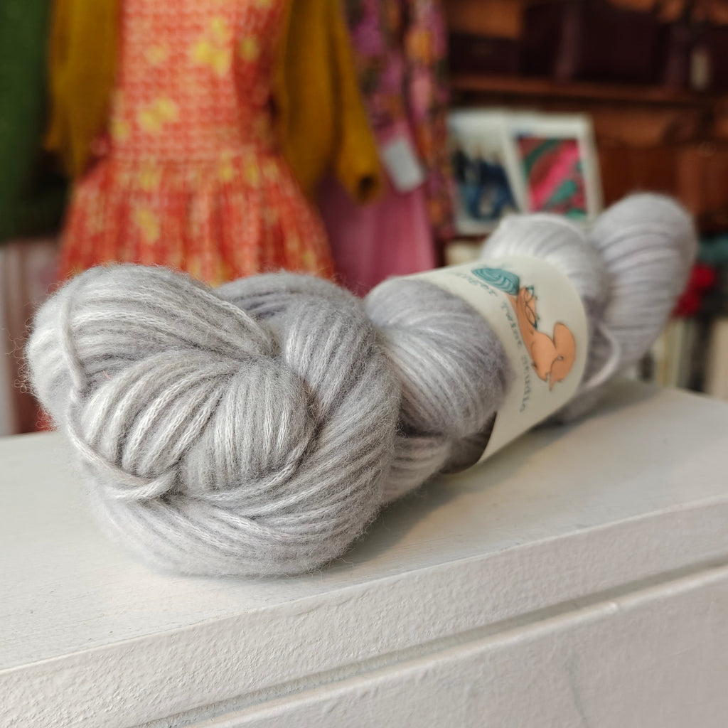 Two skeins of gray yarn on a white surface with a blurred background