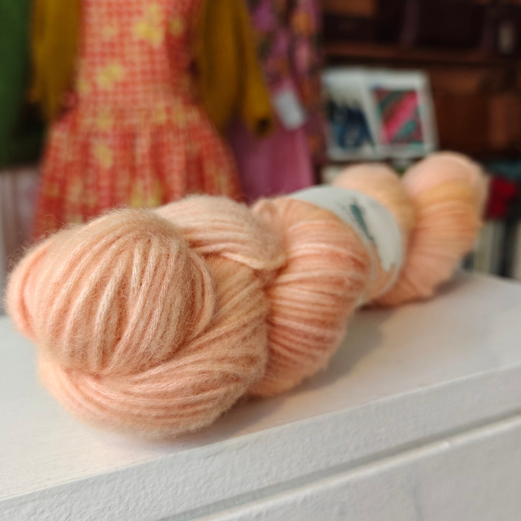 Three skeins of peach-colored yarn on a white surface with a blurred background