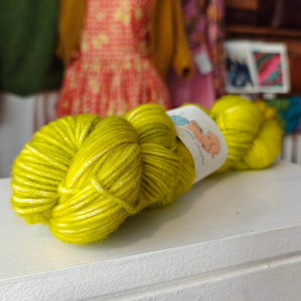 Yellow yarn skein with a label on a white surface, with blurred colorful background