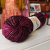 Maroon skein of yarn with a label on a white surface, blurred background