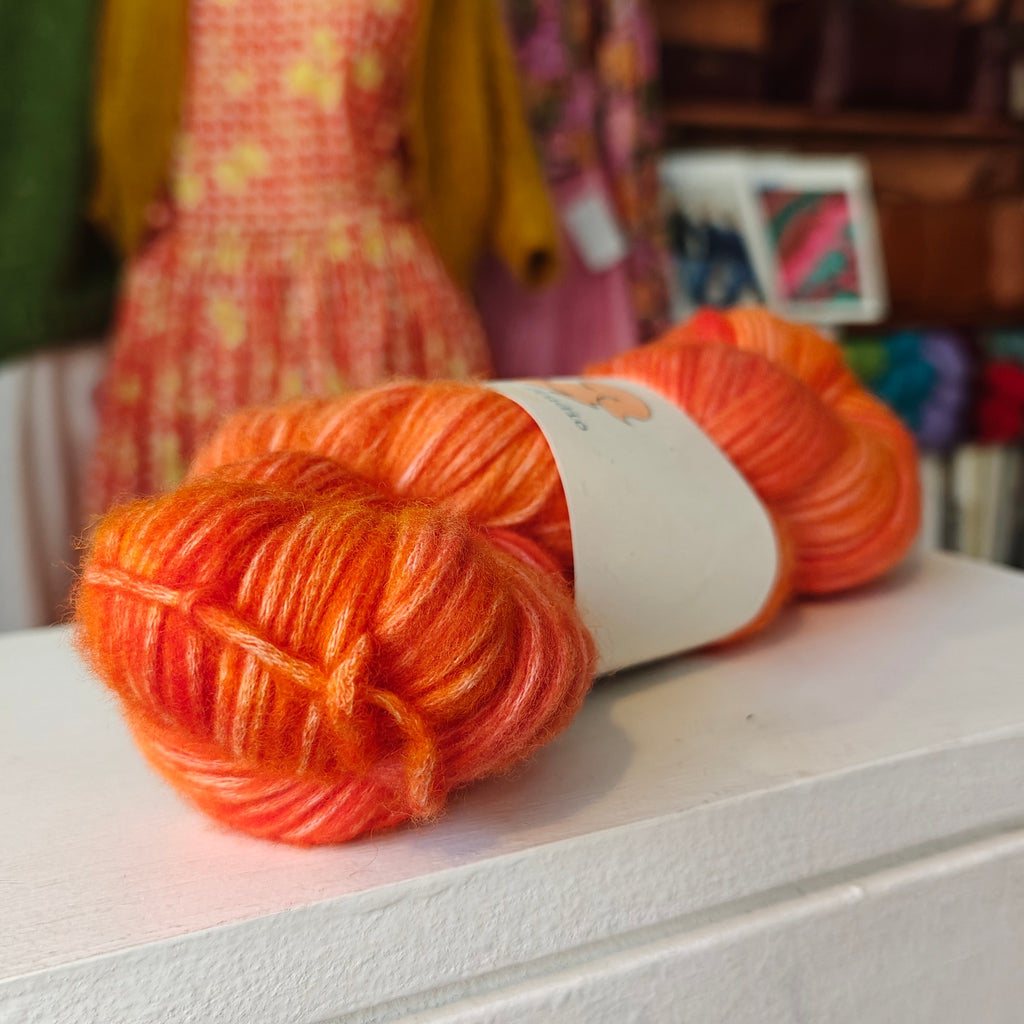 Two skeins of orange yarn on a white surface with a blurred background