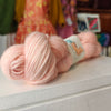 Two pink skeins of yarn on a white surface with a blurred colorful background