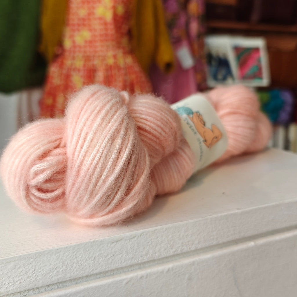 Two pink skeins of yarn on a white surface with a blurred colorful background