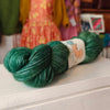Green skein of yarn with a label on a white surface, with colorful dresses in the background.