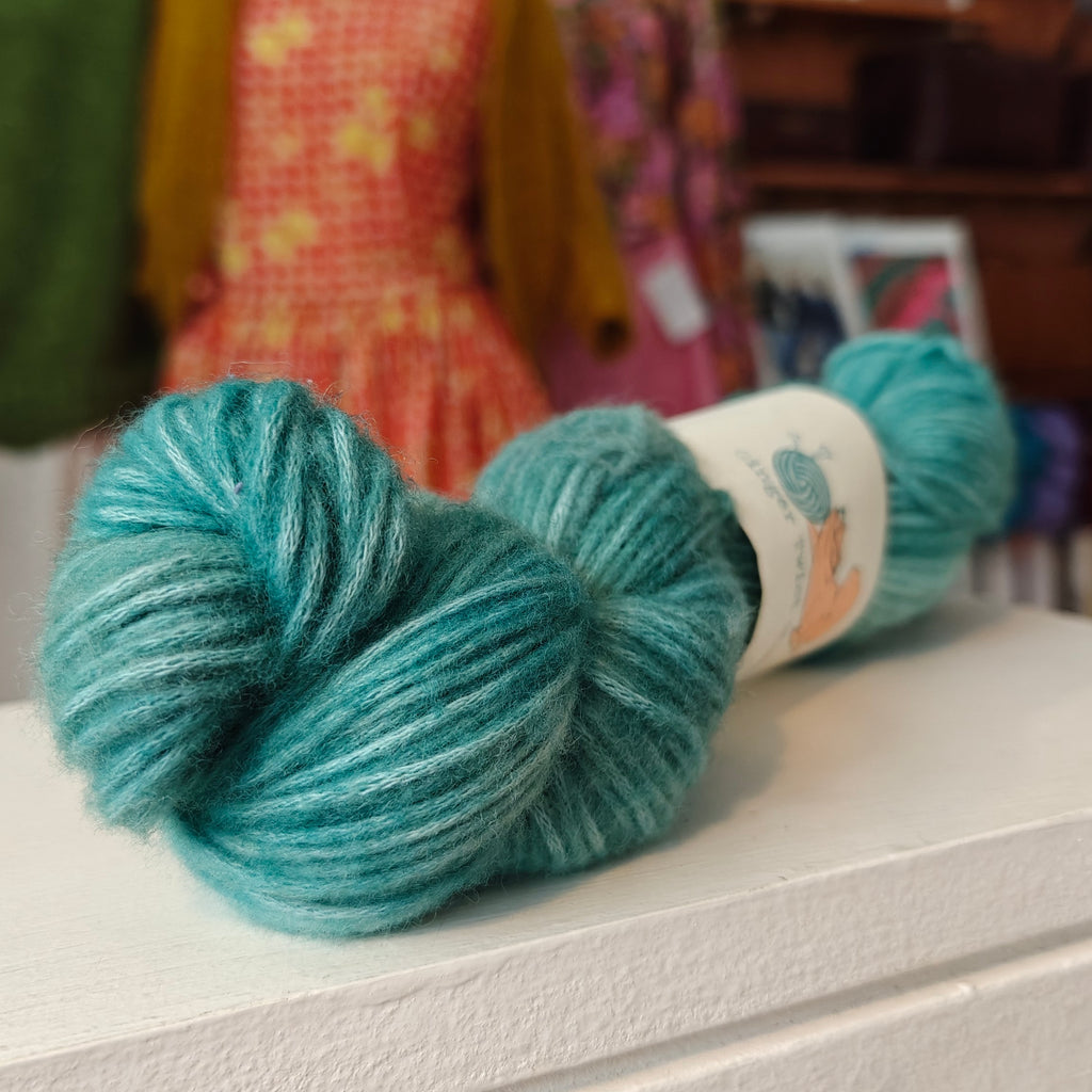 Turquoise yarn skein on a white surface with a blurred background