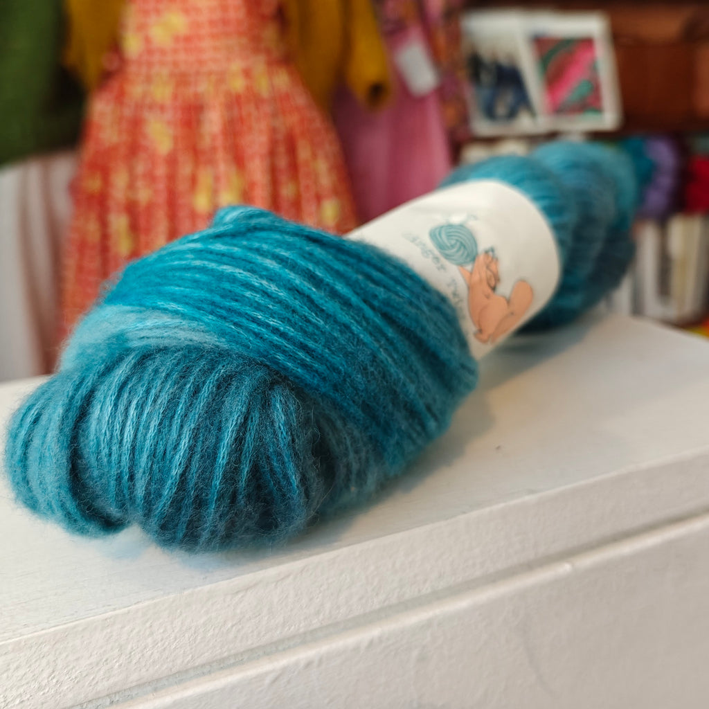 Blue skein of yarn with a label on a white surface, blurred background