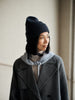 Person wearing a black knit beanie and gray coat indoors