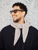 Man wearing sunglasses and a beige scarf against a textured wall