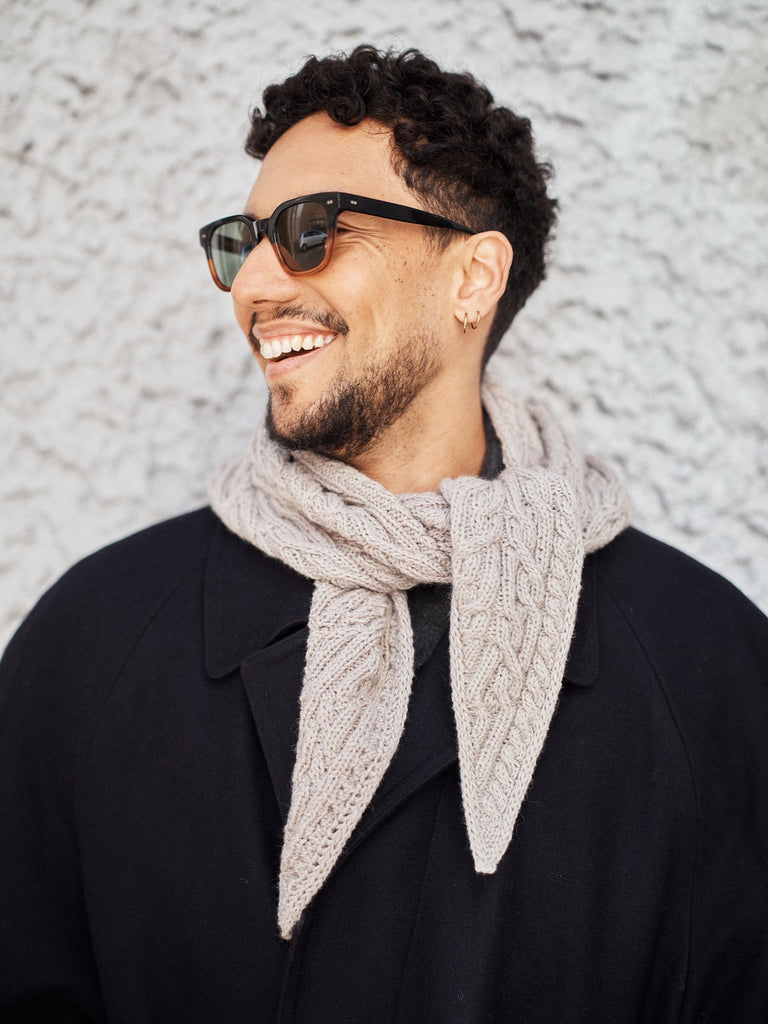 Man wearing sunglasses and a beige scarf against a textured wall