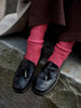 Black loafers with tassels worn with pink socks on a stone surface
