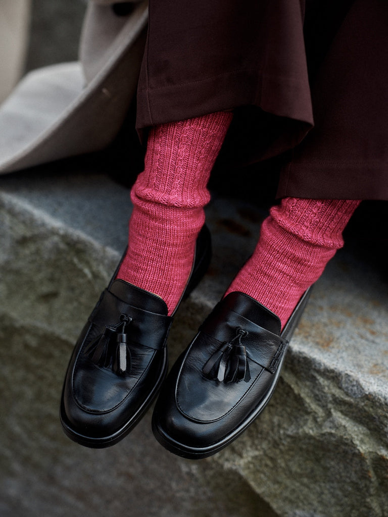 Black loafers with tassels worn with pink socks on a stone surface