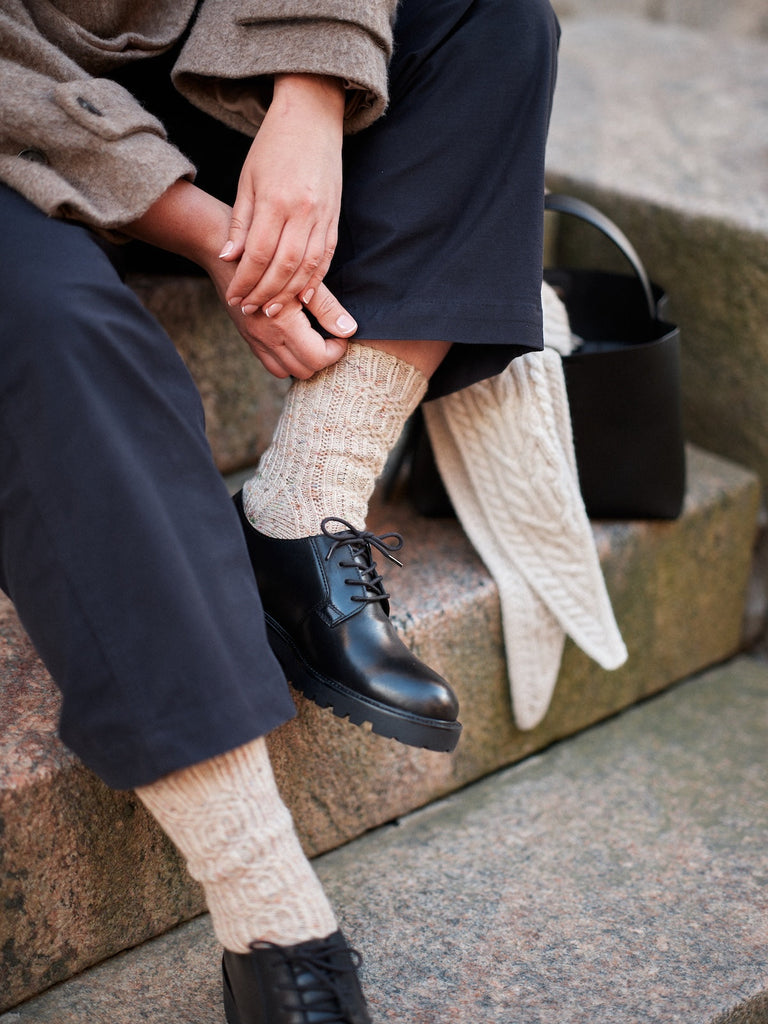 Person wearing black shoes and beige socks sitting on a stone step.