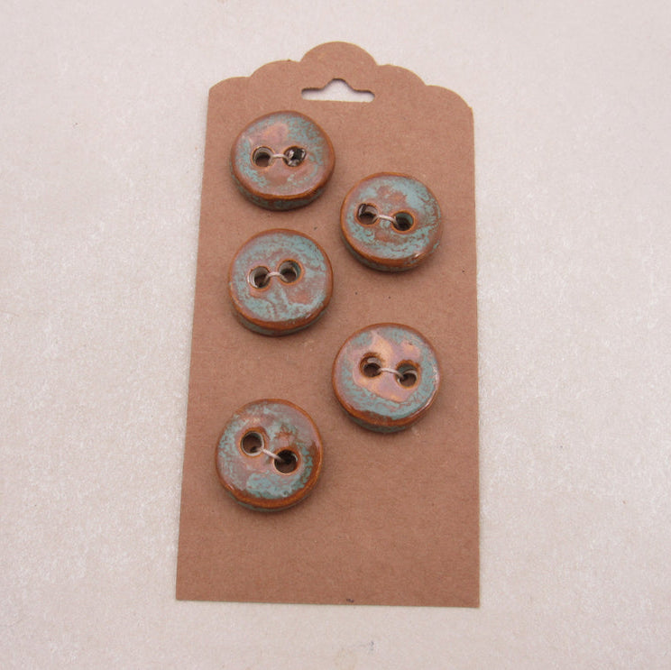 Set of five rust-colored buttons on a brown cardboard backing against a light pink background