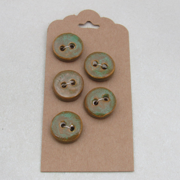 Set of four ceramic buttons with a greenish patina on a cardboard backing.
