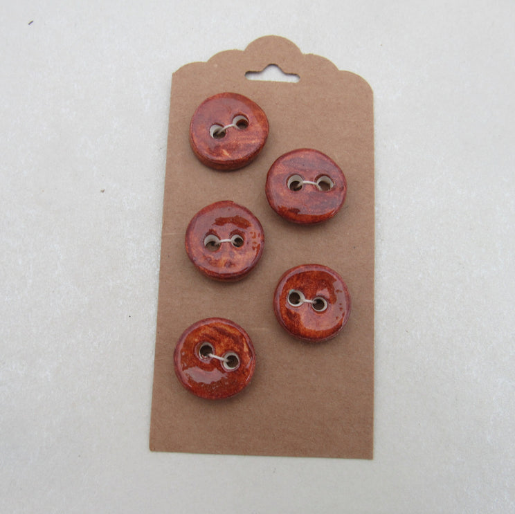 Set of five red buttons on a brown cardboard backing against a white background