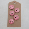 Five pink buttons on a cardboard backing with a hook, on a light gray background