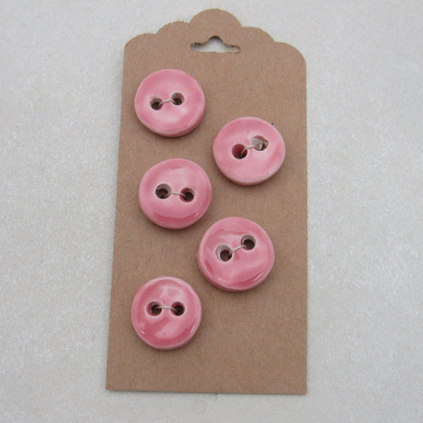 Five pink buttons on a cardboard backing with a hook, on a light gray background