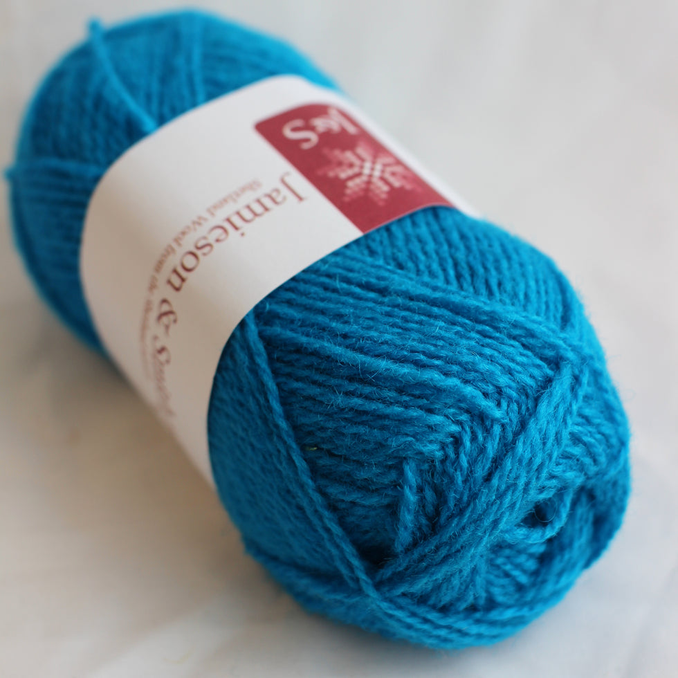 A close-up of a bright turquoise blue skein of yarn wrapped in a white paper label with a red logo, set against a soft white fabric background.