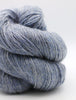 A close-up of a twisted skein of fuzzy yarn in a heathered dusty blue-gray color, set against a clean white background.