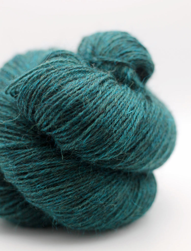 A close-up of a skein of teal yarn with a soft, fuzzy texture on a light gray background.