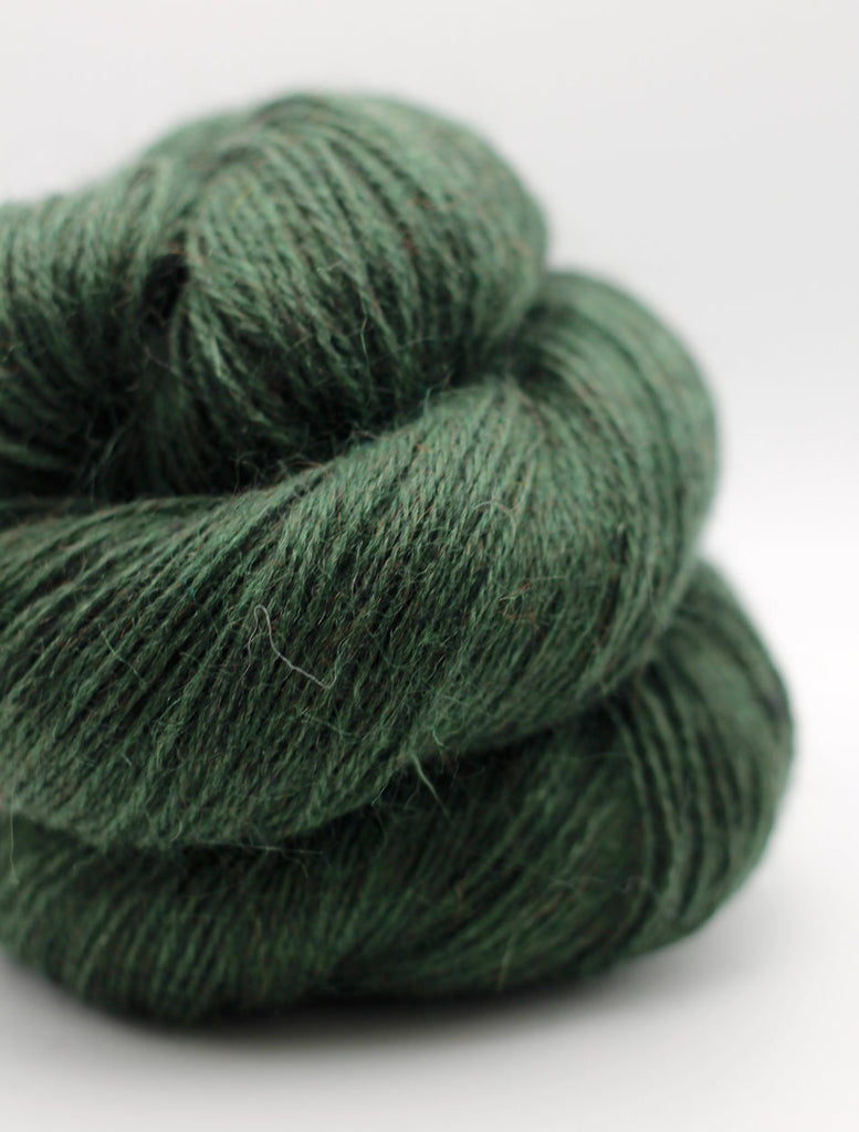 A close-up of a skein of dark forest green yarn with a soft, fuzzy texture, photographed on a clean white background.
