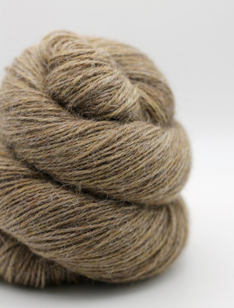 A close-up of a skein of textured yarn in a warm taupe-brown color, photographed on a clean white background.