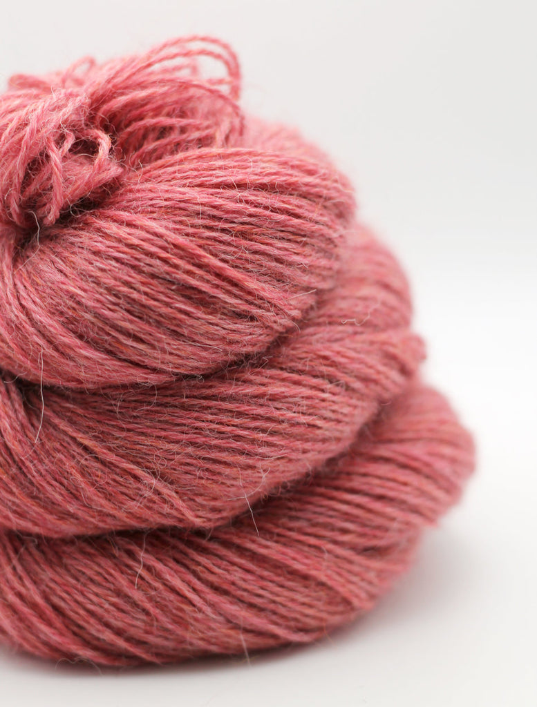 A close-up of a skein of dusty rose pink yarn on a clean white background.
