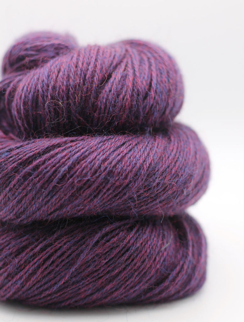 A close-up of three stacked skeins of variegated yarn in a deep purple and magenta colorway, set against a clean white background.